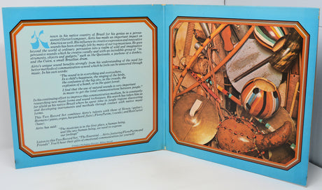 An open book or booklet spread showing two illustrated pages with text on the left and a colorful photograph of traditional drums on the right, set against a plain white background.