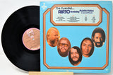A vinyl record partially pulled from its sleeve, showing the black disc and the front cover artwork. The cover is light blue with orange border lines and circular portraits of artists, including Airto and Florapurim.