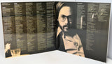 An open vinyl record sleeve or booklet showing printed track listings and a black-and-white portrait of a bearded man with glasses on the right page, photographed against a plain light background.