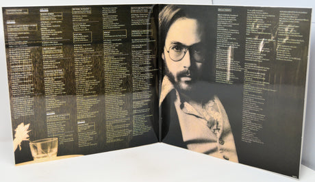 An open vinyl record sleeve or booklet showing printed track listings and a black-and-white portrait of a bearded man with glasses on the right page, photographed against a plain light background.