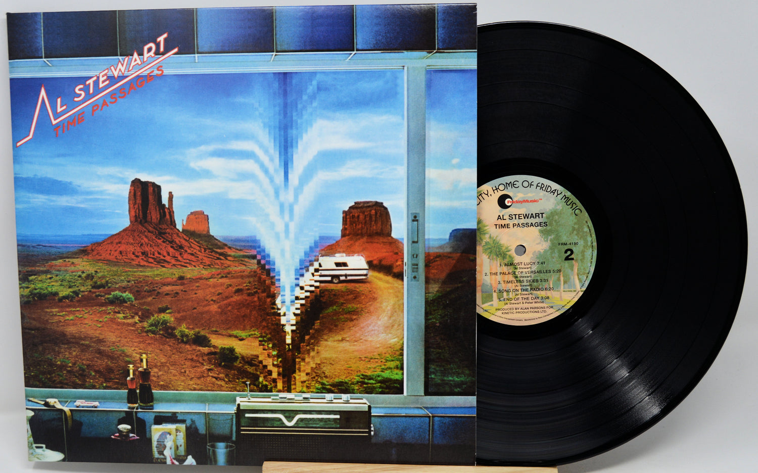 A vinyl record and its album cover for Al Stewart's 'Time Passages'. The cover features a surreal desert landscape with a white car driving down a road toward a bright light, while the black vinyl record is partially pulled out on the right.