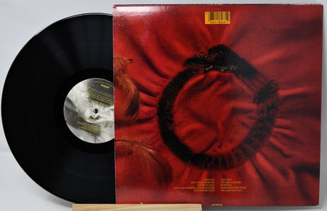 A vinyl record partially pulled from its album cover, showing a black record on the left and the cover on the right with a red abstract design and a black circular motif. The record label reads Columbia Records.
