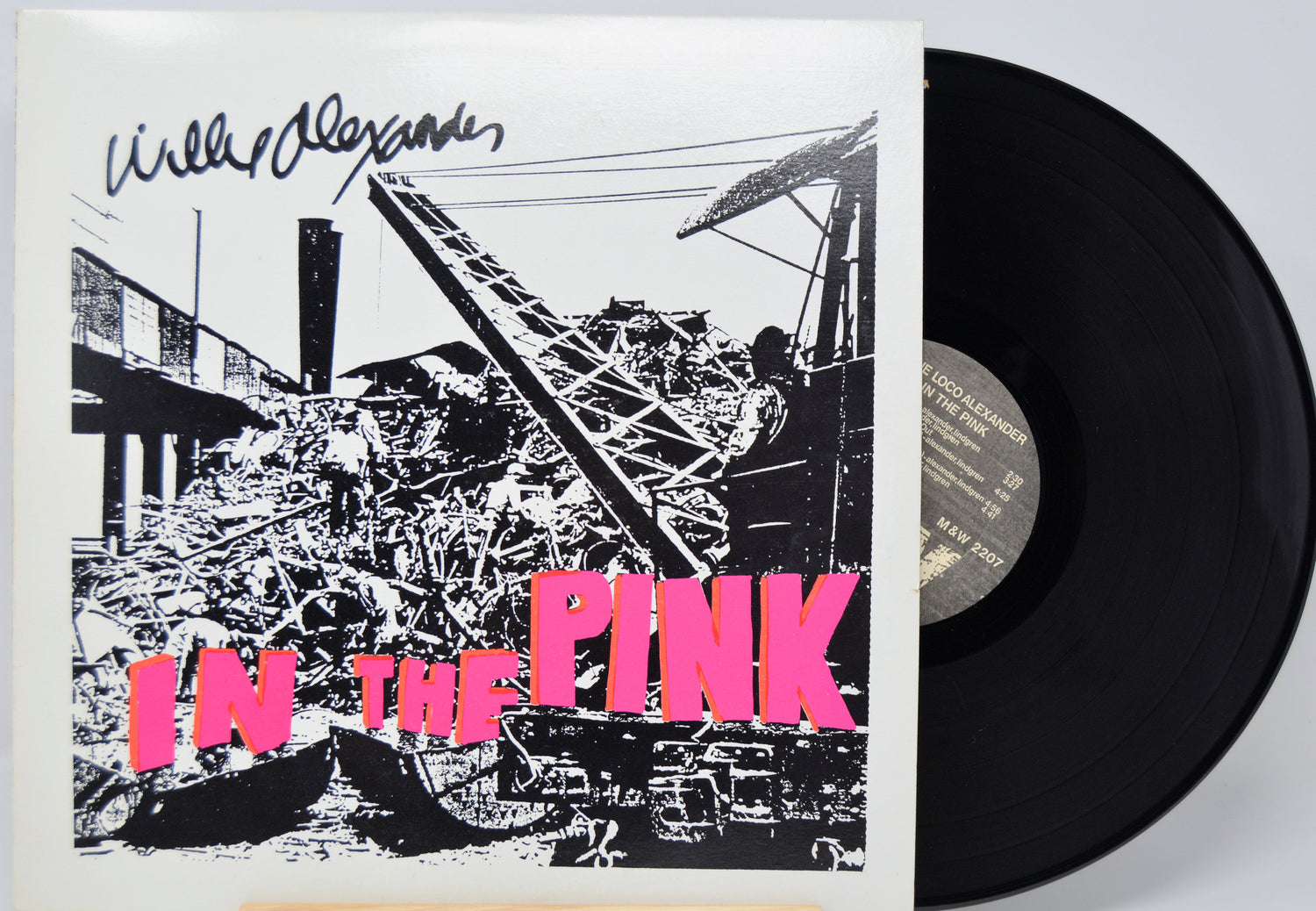 Vinyl record artwork featuring a pile of metal trash and a crane with pink lettering