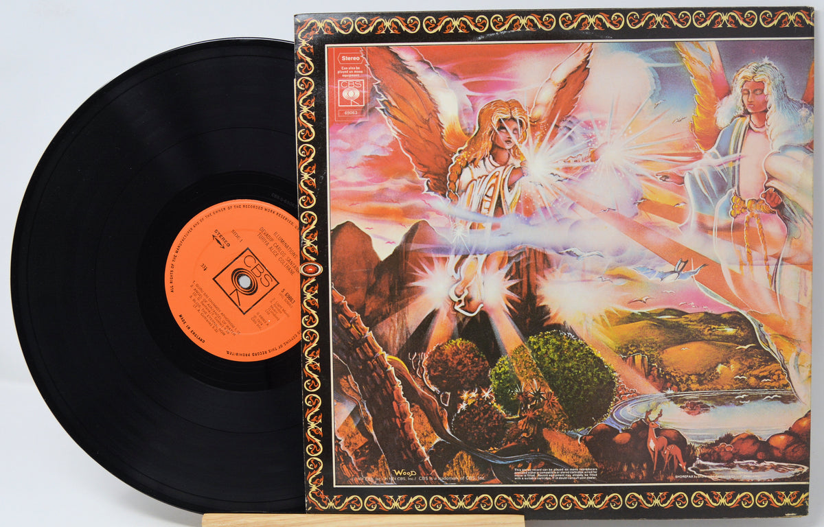 A vinyl record partially pulled from its illustrated album cover, showing a black record with an orange center label beside a square cover featuring a fantasy scene with angels and a landscape.