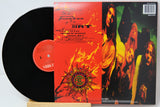 A vinyl record album shown with the black record partially pulled from its sleeve, photographed on a white background. The sleeve features a fiery red-orange front cover with a central circular logo and a photo of four band members on the right side.