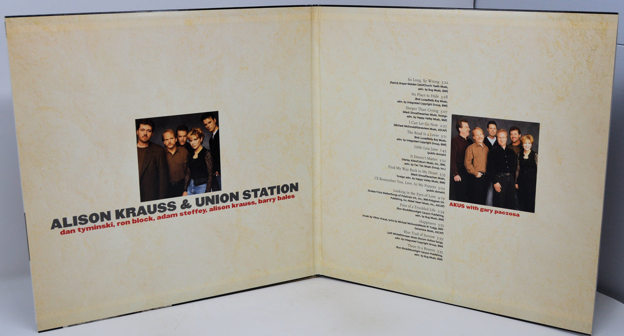 An open printed booklet or album insert with cream-colored pages, showing a small group photo, text, and song listings. The visible title reads 'ALISON KRAUSS & UNION STATION' with smaller text below.