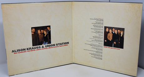 An open printed booklet or album insert with cream-colored pages, showing a small group photo, text, and song listings. The visible title reads 'ALISON KRAUSS & UNION STATION' with smaller text below.