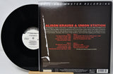 A vinyl record partially pulled from its back cover sleeve, showing the black disc on the left and the printed back of the album case on the right. The sleeve is dark brown/black with red and white text reading 'Alison Krauss & Union Station' and 'Original Master Recording.