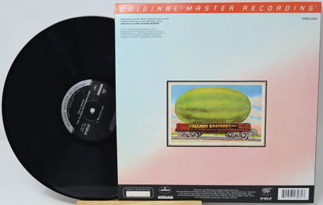 A vinyl record partially pulled from its sleeve, showing the black record on the left and the back cover of the album on the right. The sleeve features a pale blue-to-pink gradient background with a central illustration of a green oval shape on a train car labeled 'Allion Brothers.