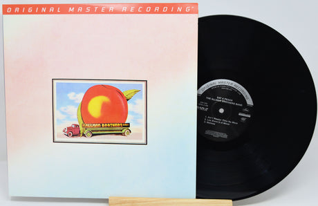 Vinyl record album with the cover partially pulled from its sleeve, showing a black LP disc beside a pastel cover featuring a framed illustration of a red apple truck.