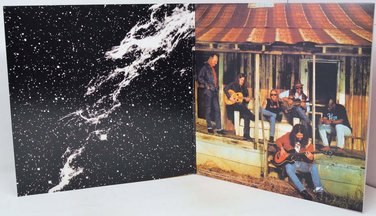 A square art print or poster displayed open against a white background, showing a split design: the left half is a black starry sky with a white nebula-like streak, and the right half shows a vintage photo of a band sitting on a porch under a rusted corrugated metal roof.