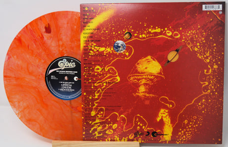 A vinyl record package shown with the orange marbled record partially visible behind the printed album cover. The cover is predominantly red and orange with yellow abstract splatter graphics and a mushroom illustration.