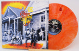 The Human Family's 'We're All Goin' Down the Road' vinyl record album with its illustrated cover sleeve and a translucent orange record partially visible behind it.