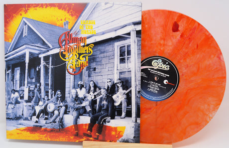 The Human Family's 'We're All Goin' Down the Road' vinyl record album with its illustrated cover sleeve and a translucent orange record partially visible behind it.
