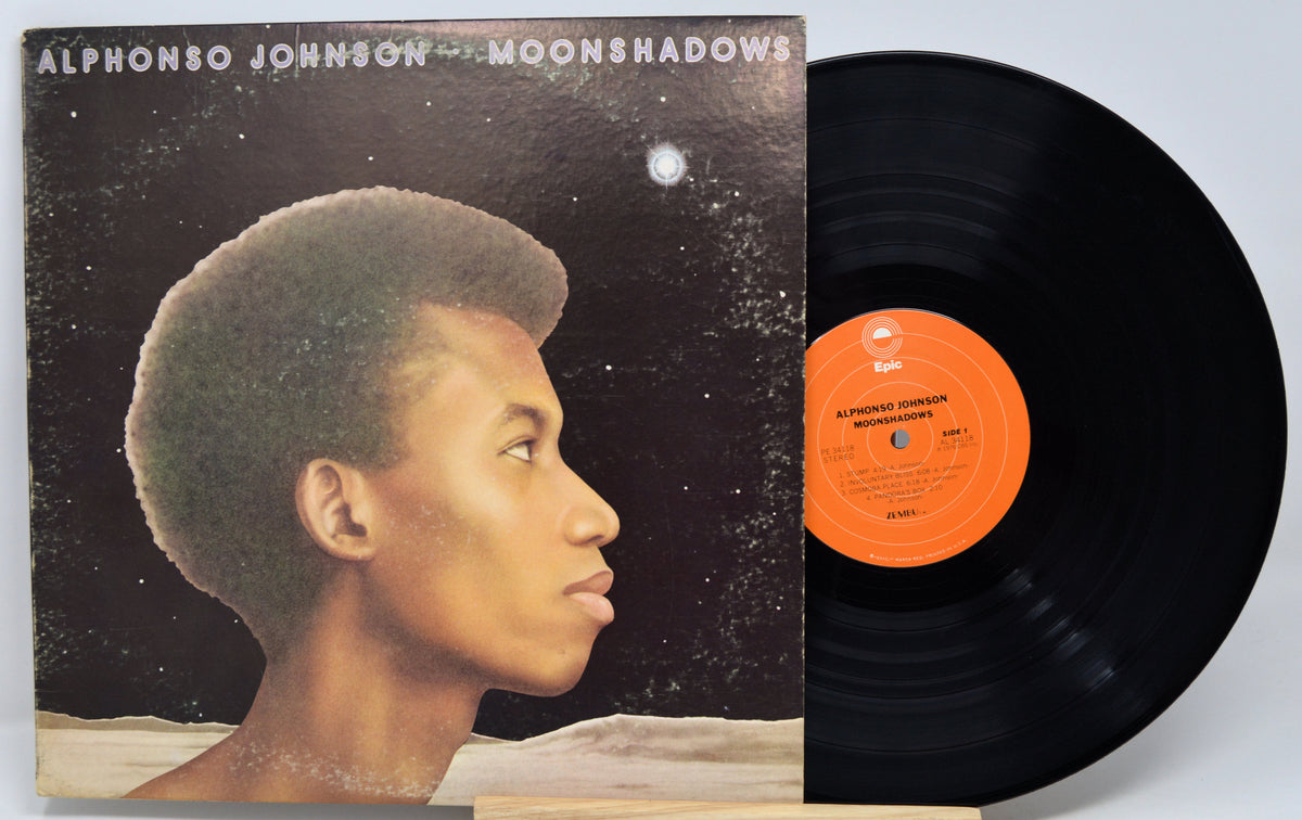 Alphonso Johnson's Moonshadows vinyl record LP with its illustrated album cover and the black record partially pulled out, showing the orange center label.