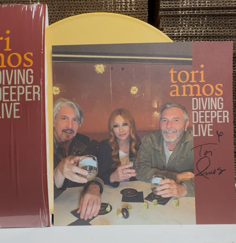 Album cover for 'Tori Amos Diving Deeper Live' with a photo of three people at a table.