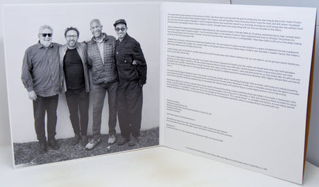 An open printed booklet or book spread showing a black-and-white group photograph of four men on the left page and columns of small text on the right page, photographed against a light neutral background.