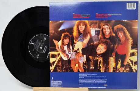 A vinyl record partially pulled from its blue cardboard sleeve, showing the black record on the left and the back cover artwork on the right. The sleeve features a band photo with multiple people and text tracks at the top and bottom.