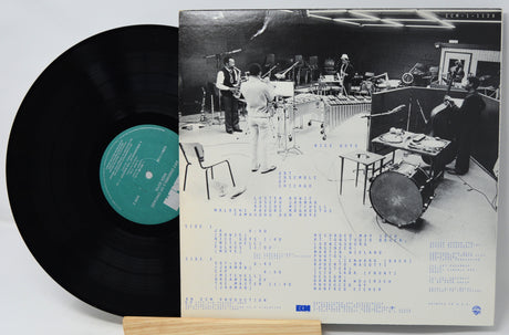 Vinyl record with a black and white album cover showing a band in a studio setting.