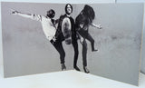 Black and white photo of three people in a dynamic pose on a textured gray background