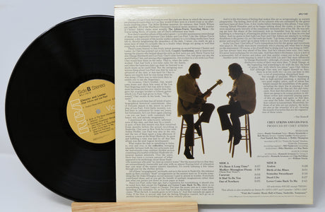 A vinyl record titled 'Chester & Lester' by Chet Atkins & Les Paul with a photo of the artists on the cover, smiling and holding guitars. The record is placed on a wooden stand.