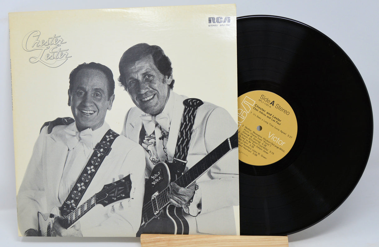 A vinyl record titled 'Chester & Lester' by Chet Atkins & Les Paul with a photo of the artists on the cover, smiling and holding guitars. The record is placed on a wooden stand.