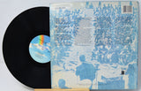 A vinyl record partially pulled from its back cover sleeve, photographed on a plain light background. The record is black with a blue-and-white center label featuring a rainbow arc.