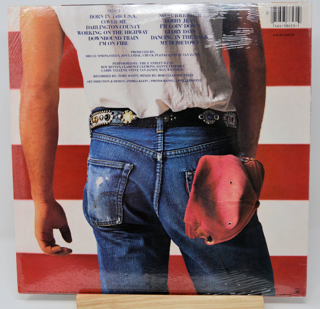 Back cover of 'Born in the U.S.A.' vinyl album showing denim jeans, a white shirt, and red cap against an American flag background
