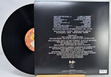 A vinyl record partially pulled from its black outer sleeve, showing the back of the packaging with track listings and a small orange label visible on the black record.