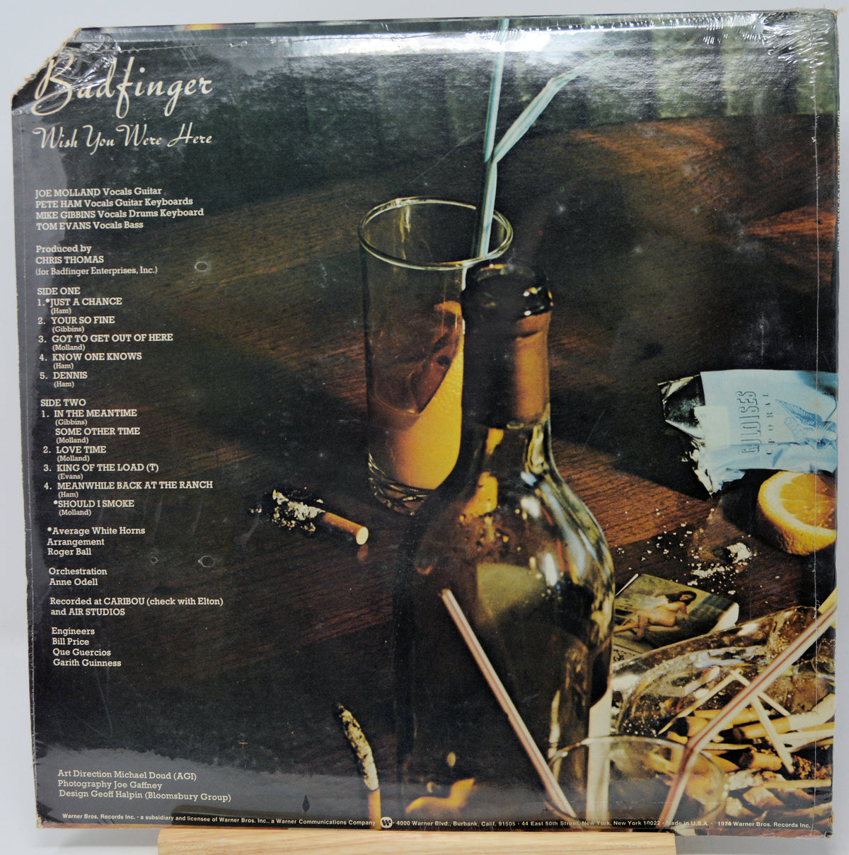 Vinyl record album cover for Badfinger's 'Pick Up Your Wine Here', showing a dark bottle, a glass with an orange drink and straw, a slice of orange, and a messy bar scene. The left side contains the tracklist.