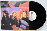 Vinyl record with a colorful cover featuring three people, displayed on a white background.