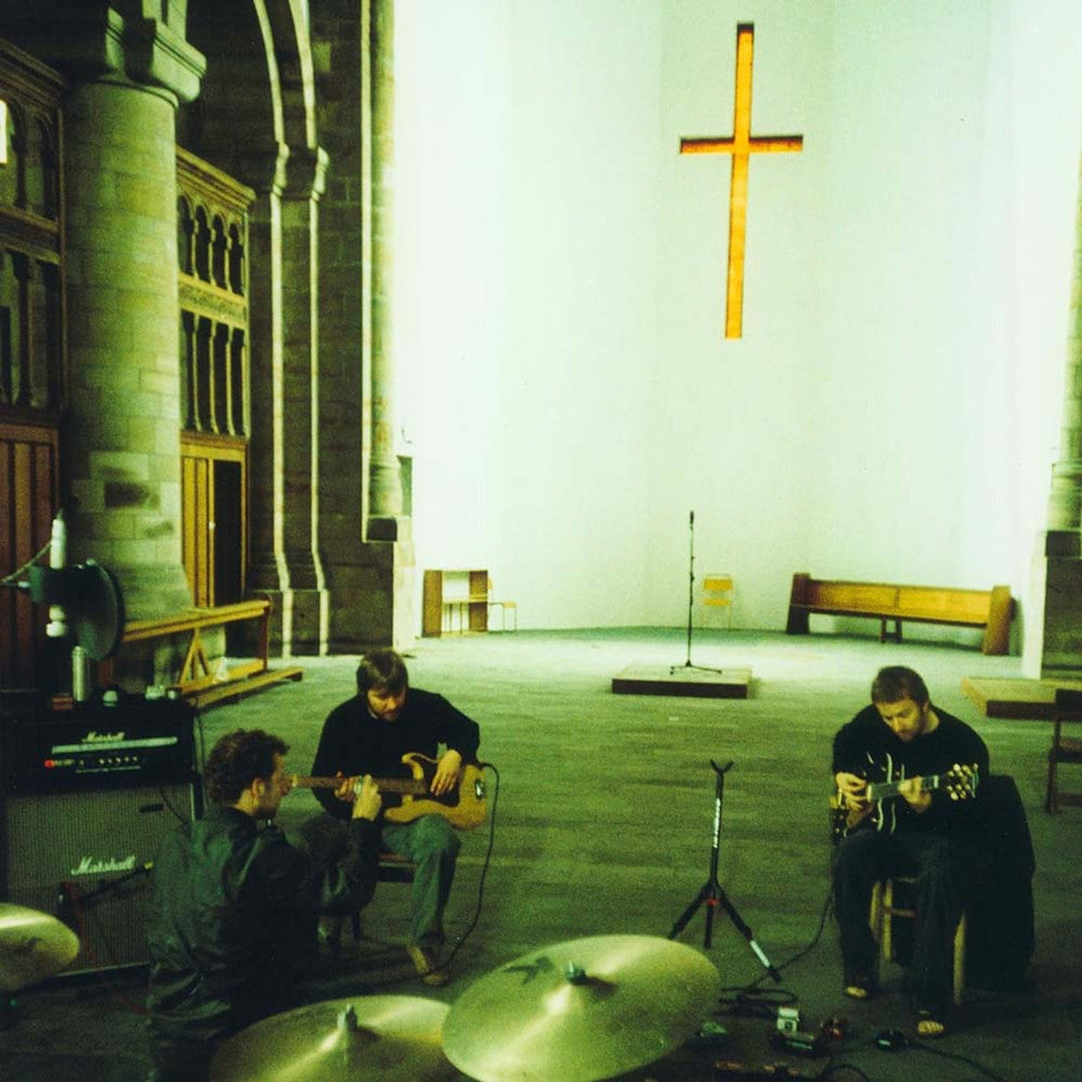 Three musicians performing with instruments inside a spacious church, illuminated by a cross-shaped window.