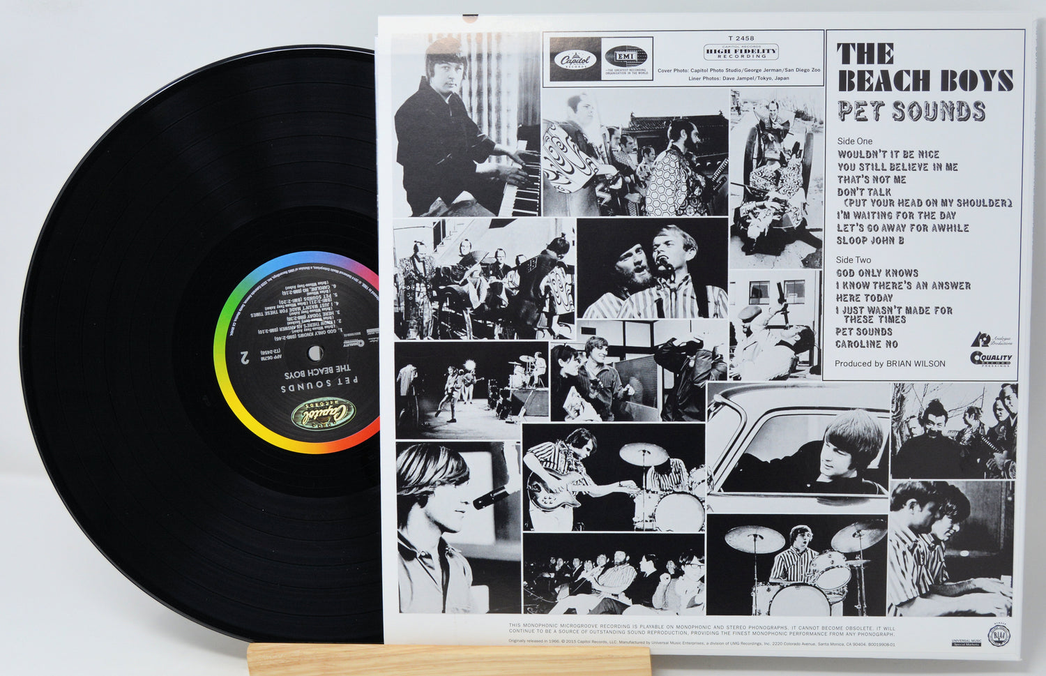 A vinyl record partially pulled from its printed album sleeve, showing the black record with a rainbow-colored center label and the back cover artwork for The Beach Boys' 'Pet Sounds'.
