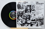 A vinyl record partially pulled from its printed album sleeve, showing the black record with a rainbow-colored center label and the back cover artwork for The Beach Boys' 'Pet Sounds'.