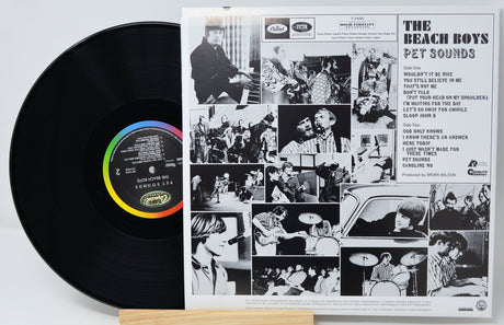 A vinyl record partially pulled from its printed album sleeve, showing the black record with a rainbow-colored center label and the back cover artwork for The Beach Boys' 'Pet Sounds'.