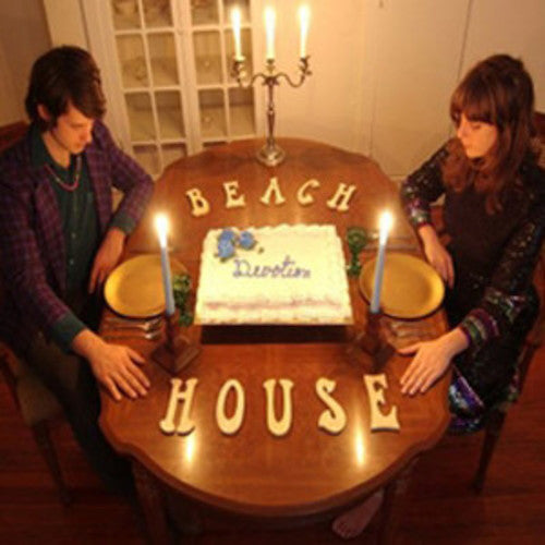 Two people sitting at a table with a cake and 'Beach House' spelled out on the table.
