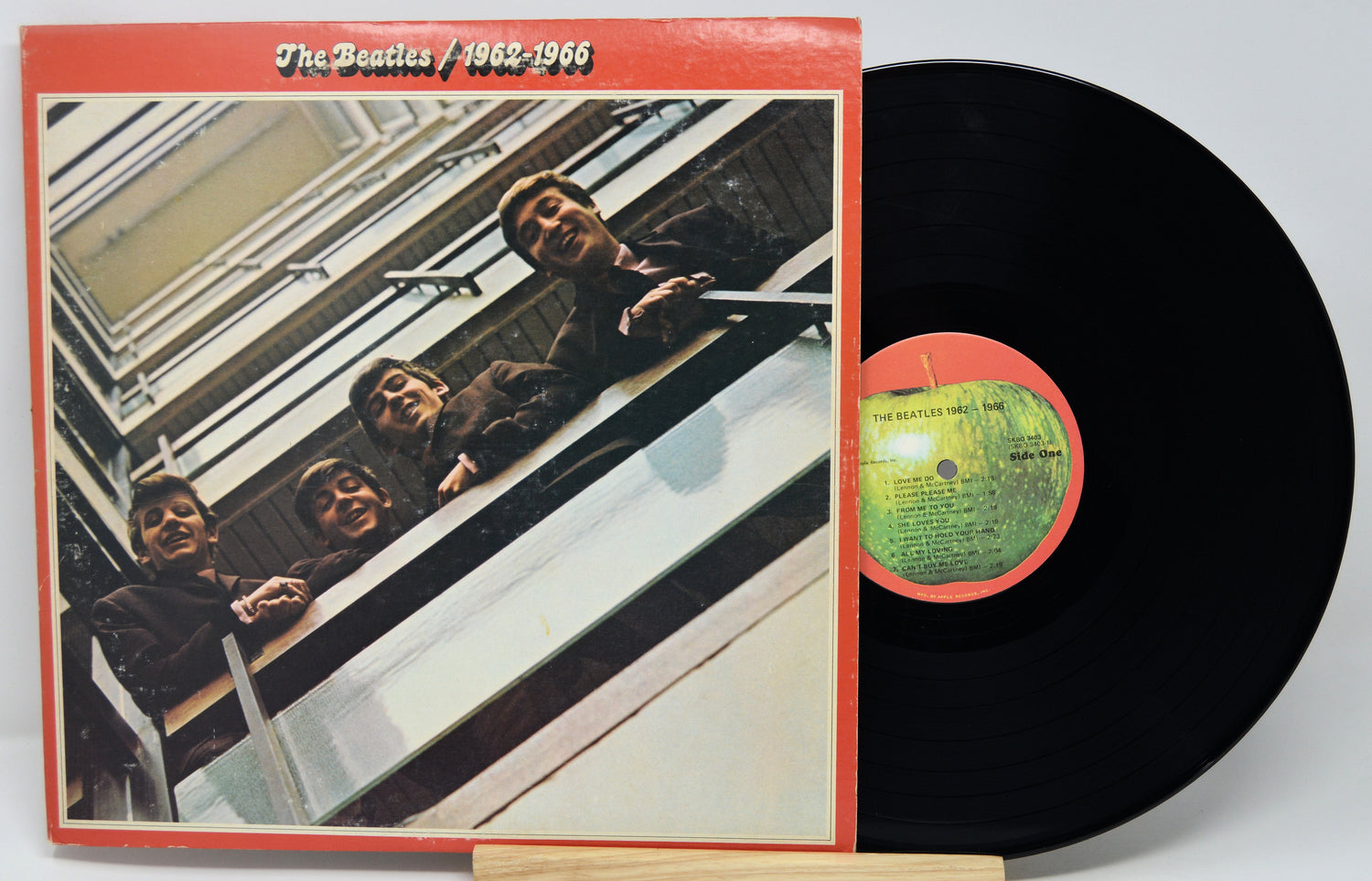 Vinyl record with cover featuring The Beatles on a staircase, on a light gray background.