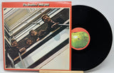 Vinyl record with cover featuring The Beatles on a staircase, on a light gray background.