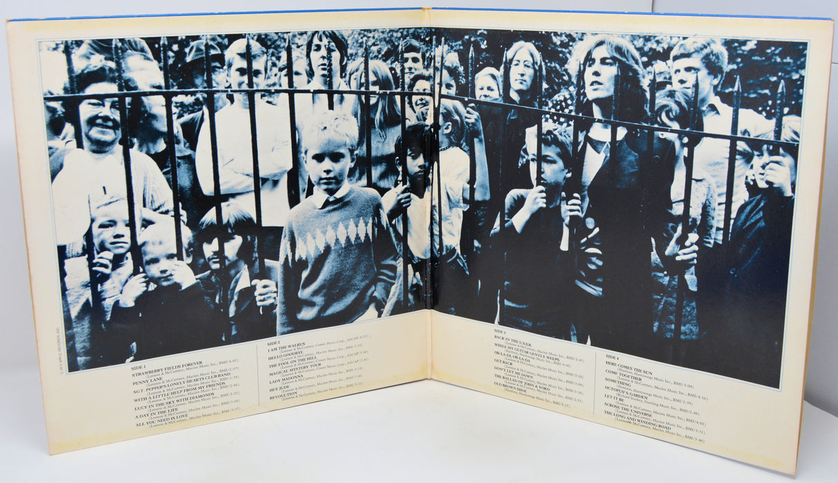 An open vintage book or photo album showing a black-and-white photograph of a crowd behind a fence, with printed text columns on the cream-colored pages.
