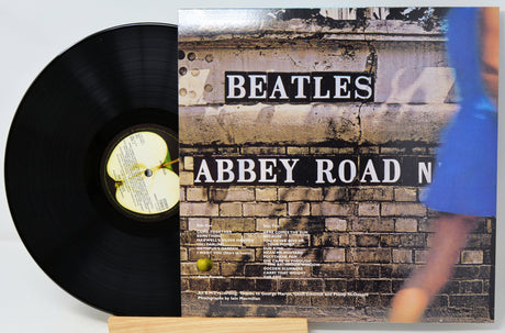 A Beatles 'Abbey Road' vinyl record partially pulled from its album cover, displayed on a small wooden stand against a light gray background.