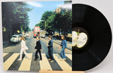 A vinyl record partially pulled from its sleeve, showing the iconic Abbey Road album cover artwork and a black record disc with a visible center label.