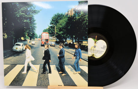 A vinyl record partially pulled from its sleeve, showing the iconic Abbey Road album cover artwork and a black record disc with a visible center label.