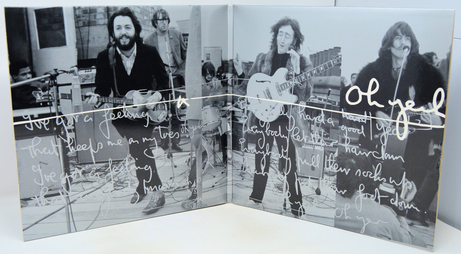 A square black-and-white printed artwork or album-cover style panel showing three musicians performing, overlaid with handwritten white text and signatures, photographed against a light neutral background.