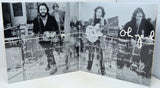 A square black-and-white printed artwork or album-cover style panel showing three musicians performing, overlaid with handwritten white text and signatures, photographed against a light neutral background.