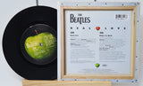 Vinyl record with a green apple graphic and a framed music sheet titled 'Real Love' by The Beatles on a white background.