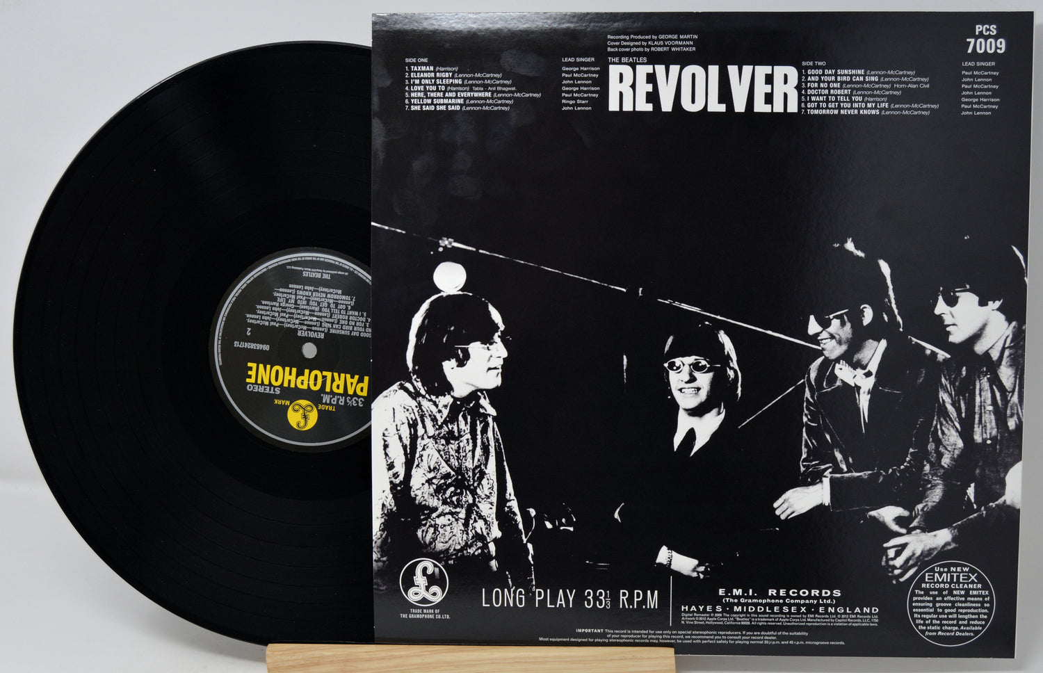 A black vinyl record partially pulled from its sleeve, showing the front cover for the band Revolver's 'Long Play 33 RPM'. The sleeve features a high-contrast black and white photo of the band members, with the band name 'REVOLVER' in bold white text at the top.