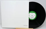 Vinyl record with a green label and white sleeve on a light gray background