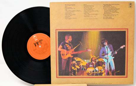 A vinyl record partially pulled from its sleeve, showing the black record with an orange label next to the tan printed album cover featuring a band photo and track listings.