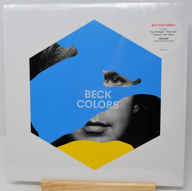 Beck Colors 'Red Vinyl Edition' LP album cover, sealed in plastic shrink wrap, displayed on a wooden stand against a white background.