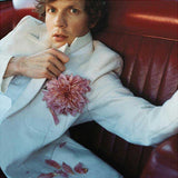 Person wearing a white coat with a pink flower, sitting on a red leather couch.